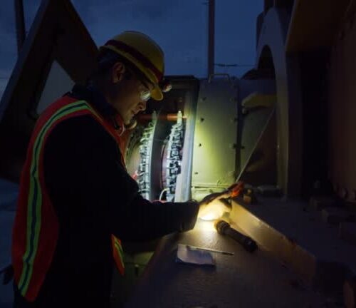 An electrician holds a flashlight to look into a generator at a power plant at night.