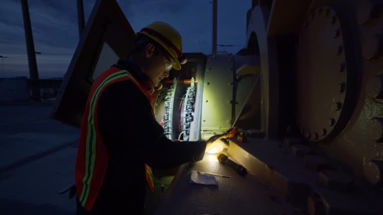 An electrician holds a flashlight to look into a generator at a power plant at night.